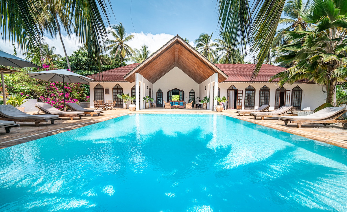 Pool with full villa facade and bougainvillea in bright sunshine